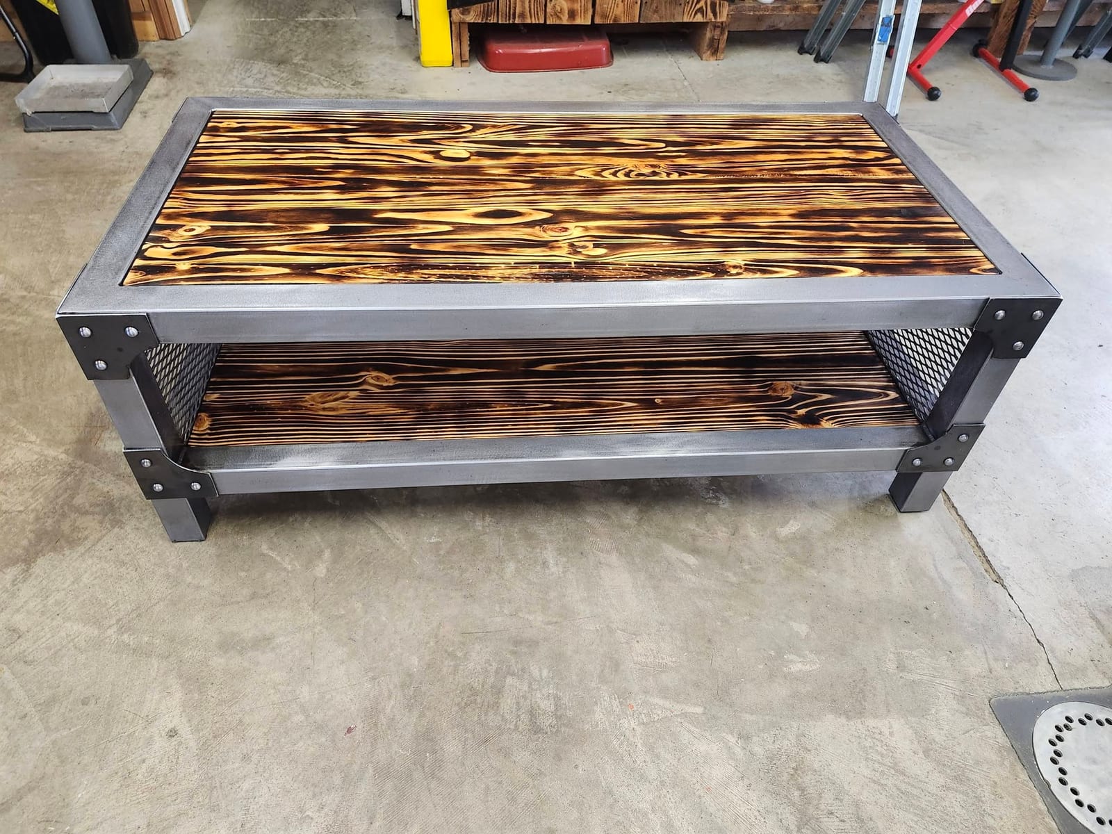 A custom coffee table with a raw steel frame, riveted corner gussets, expanded metal side panels and a torched wood top