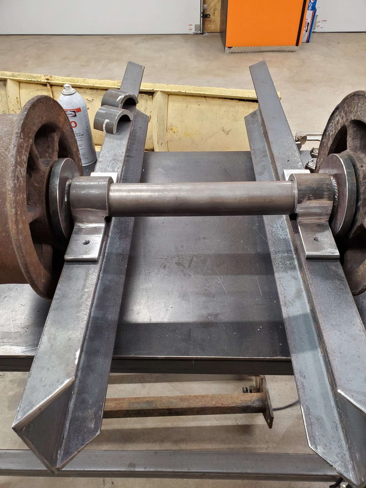 A rail cart axle under construction on the welding table, with two cast iron rail wheels welded to a round shaft between plate bearing brackets