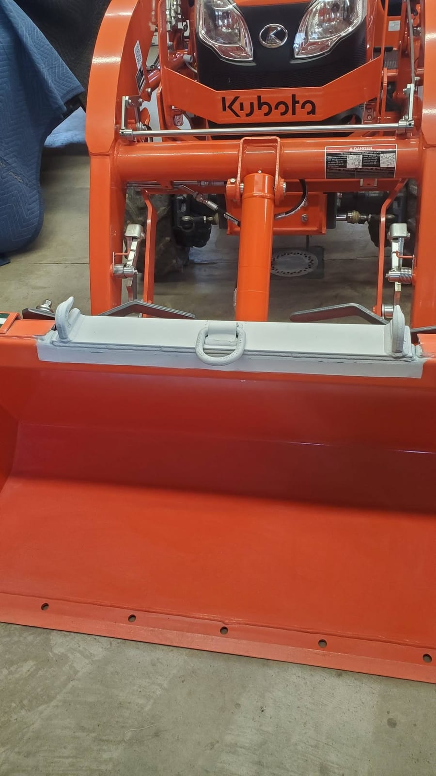 A newly welded steel top plate with two grab hooks and a center lifting ring fitted to a Kubota loader bucket