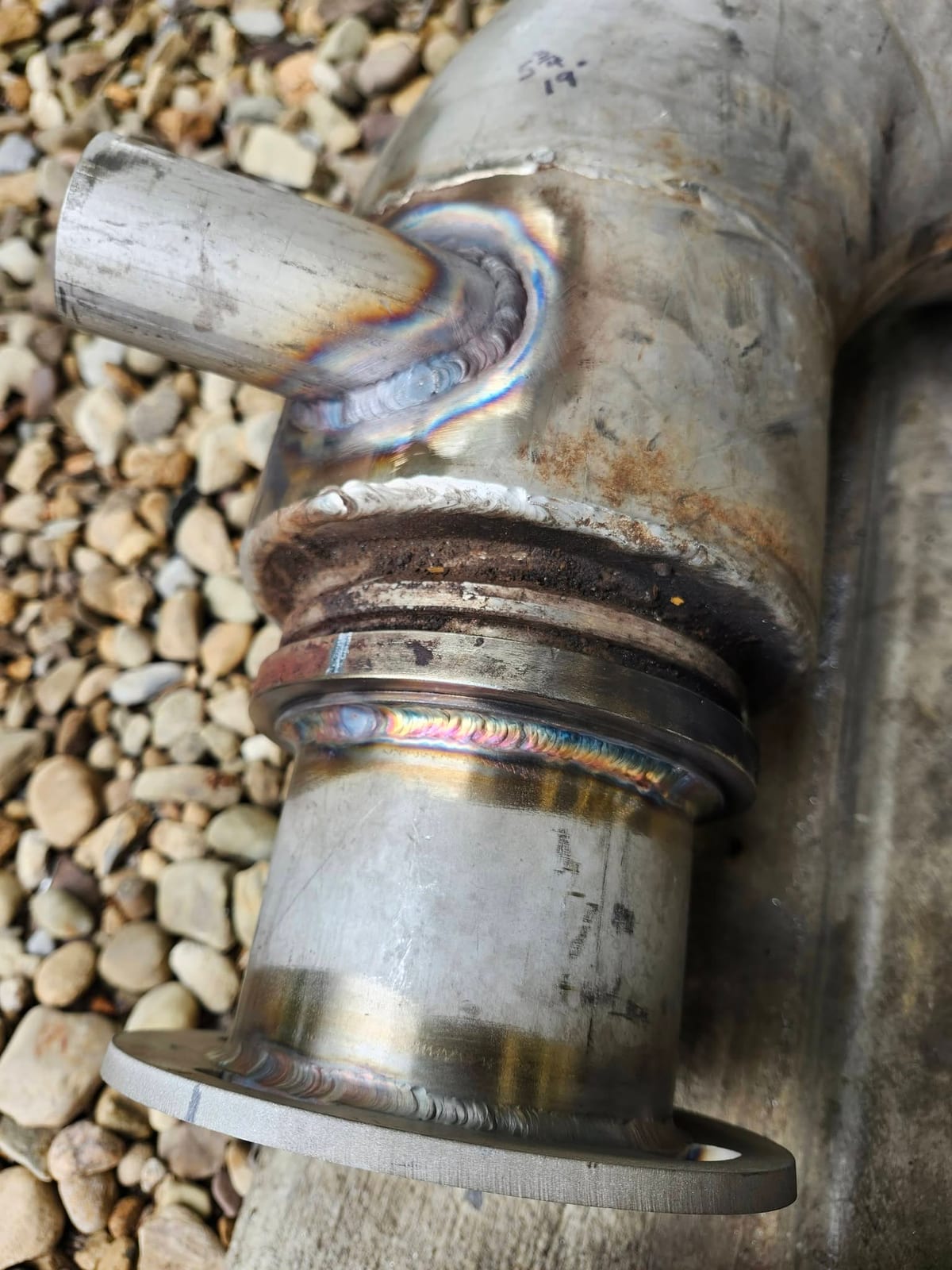 Close-up of stacked-dime TIG weld beads joining a branch stub and slip flange to a stainless pipe assembly