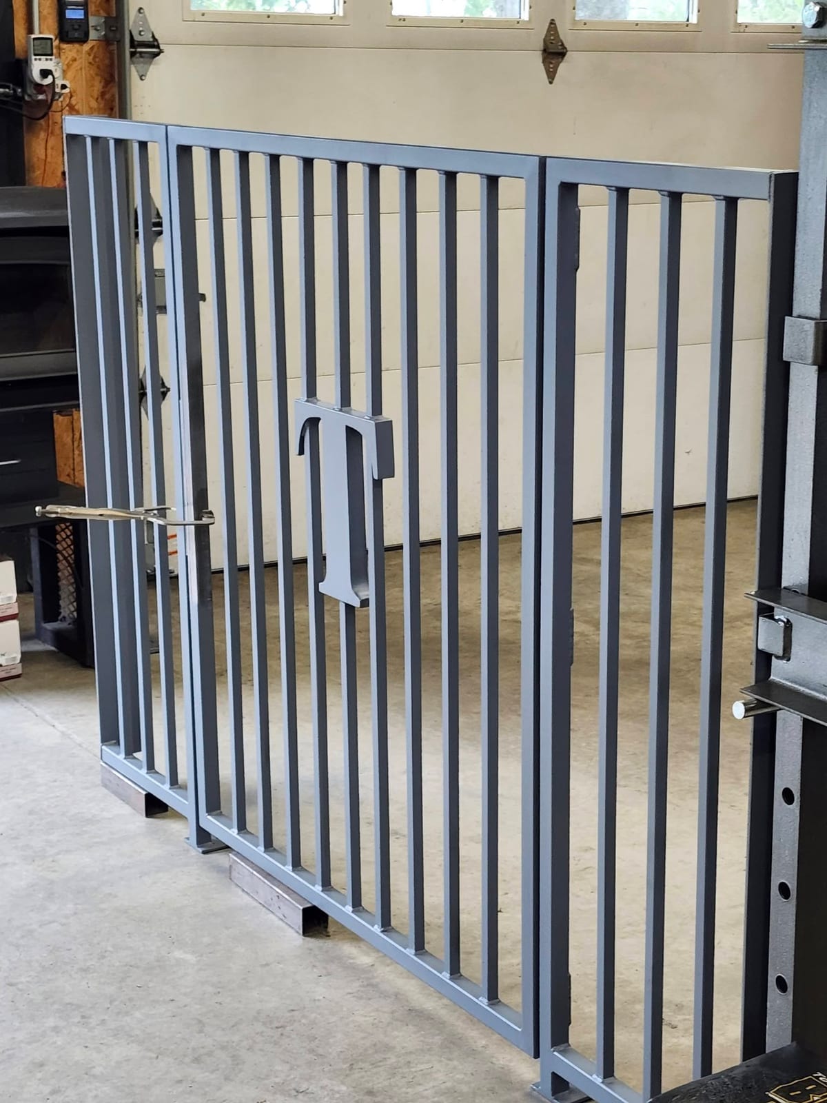 The finished custom name gate with its two side panels, painted gray and standing in front of the shop door
