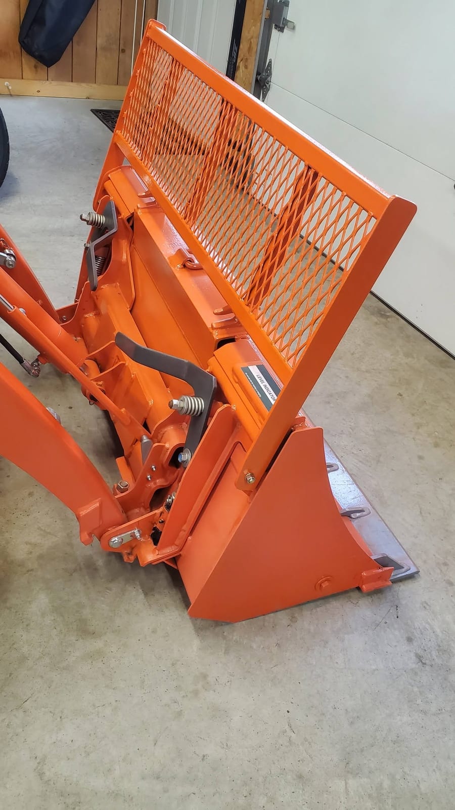 A finished orange Kubota loader bucket with a custom expanded metal guard screen welded across the top
