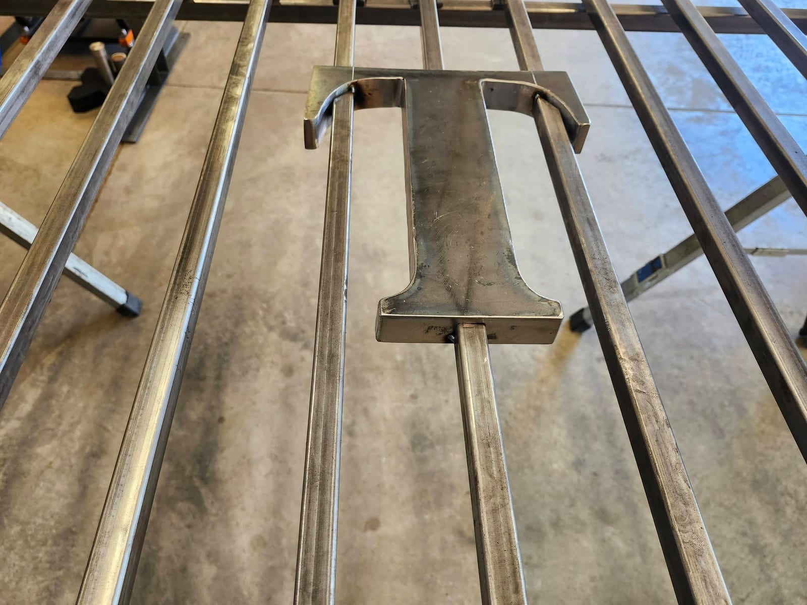 Close-up of a bare steel letter T welded between the square tube spindles of a gate before painting