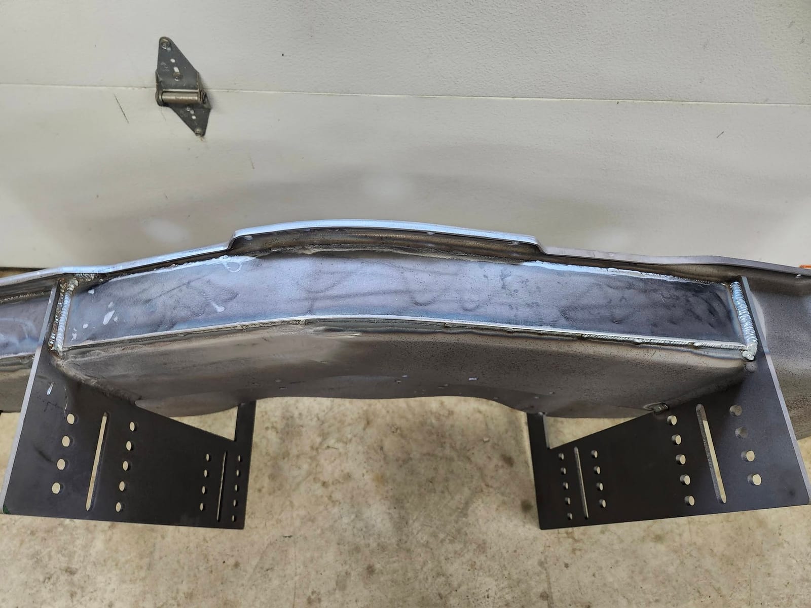 A repaired steel crossmember with new slotted mounting brackets welded to the underside