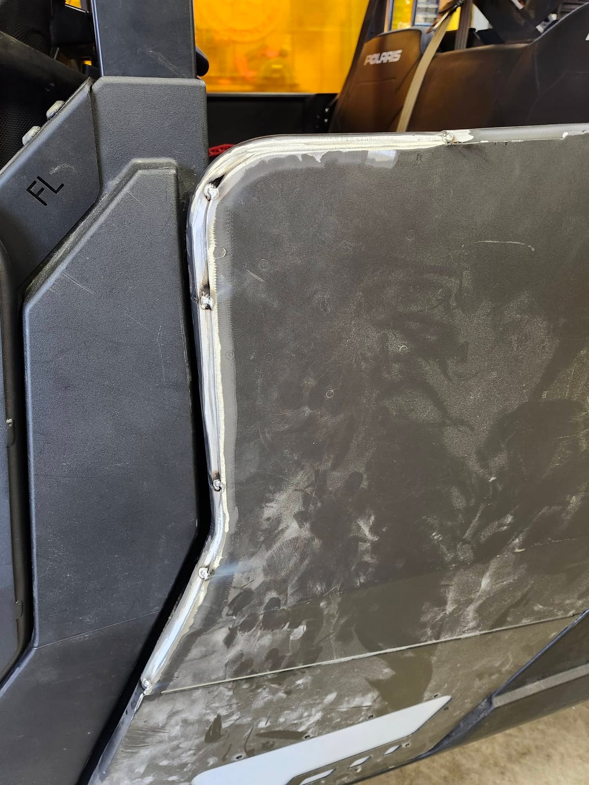 A fresh weld bead running along a replacement metal panel fitted into the door of a Polaris side-by-side