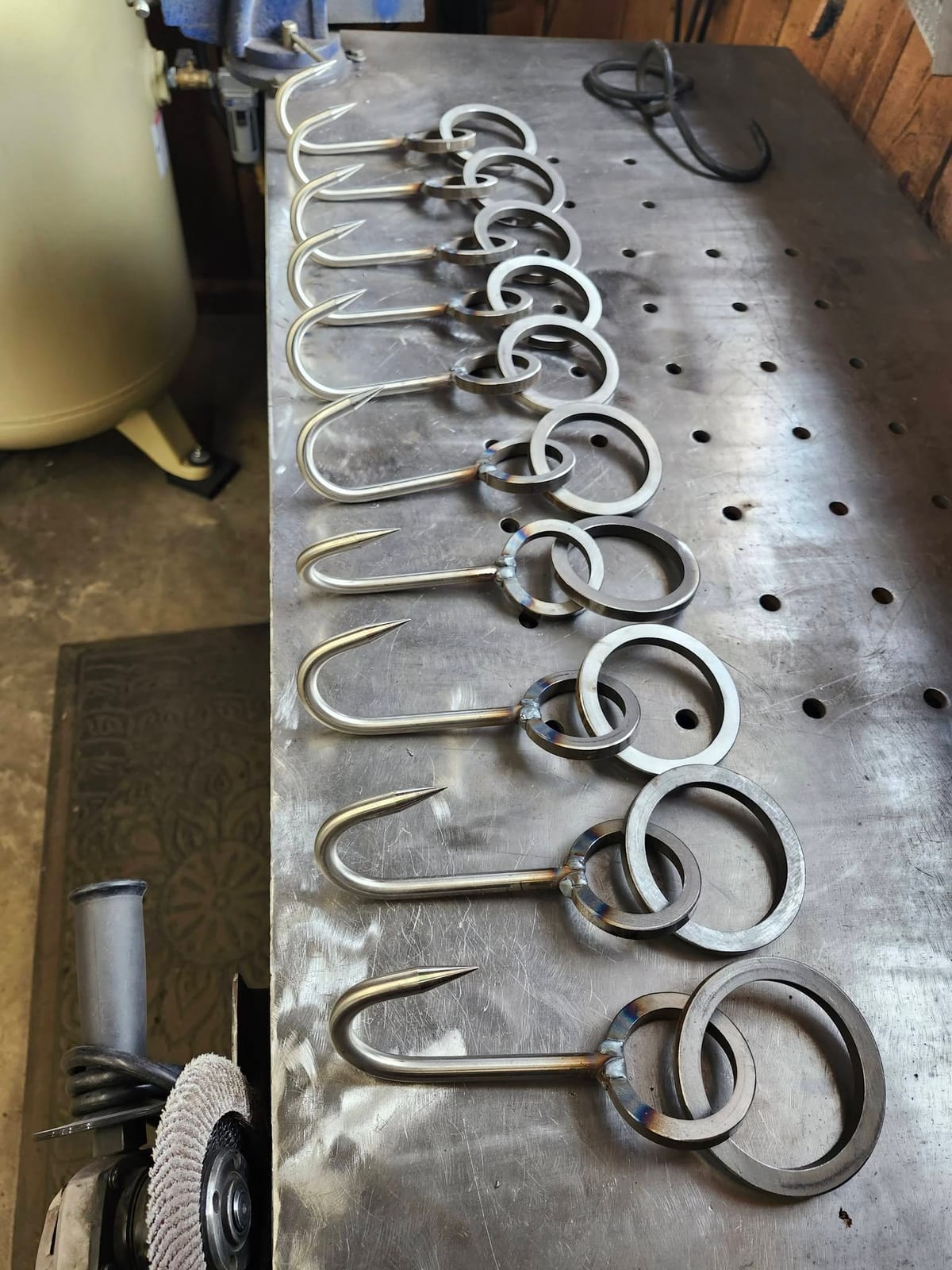 A row of a dozen hand-formed hanging hooks with welded rings laid out on the shop fixture table