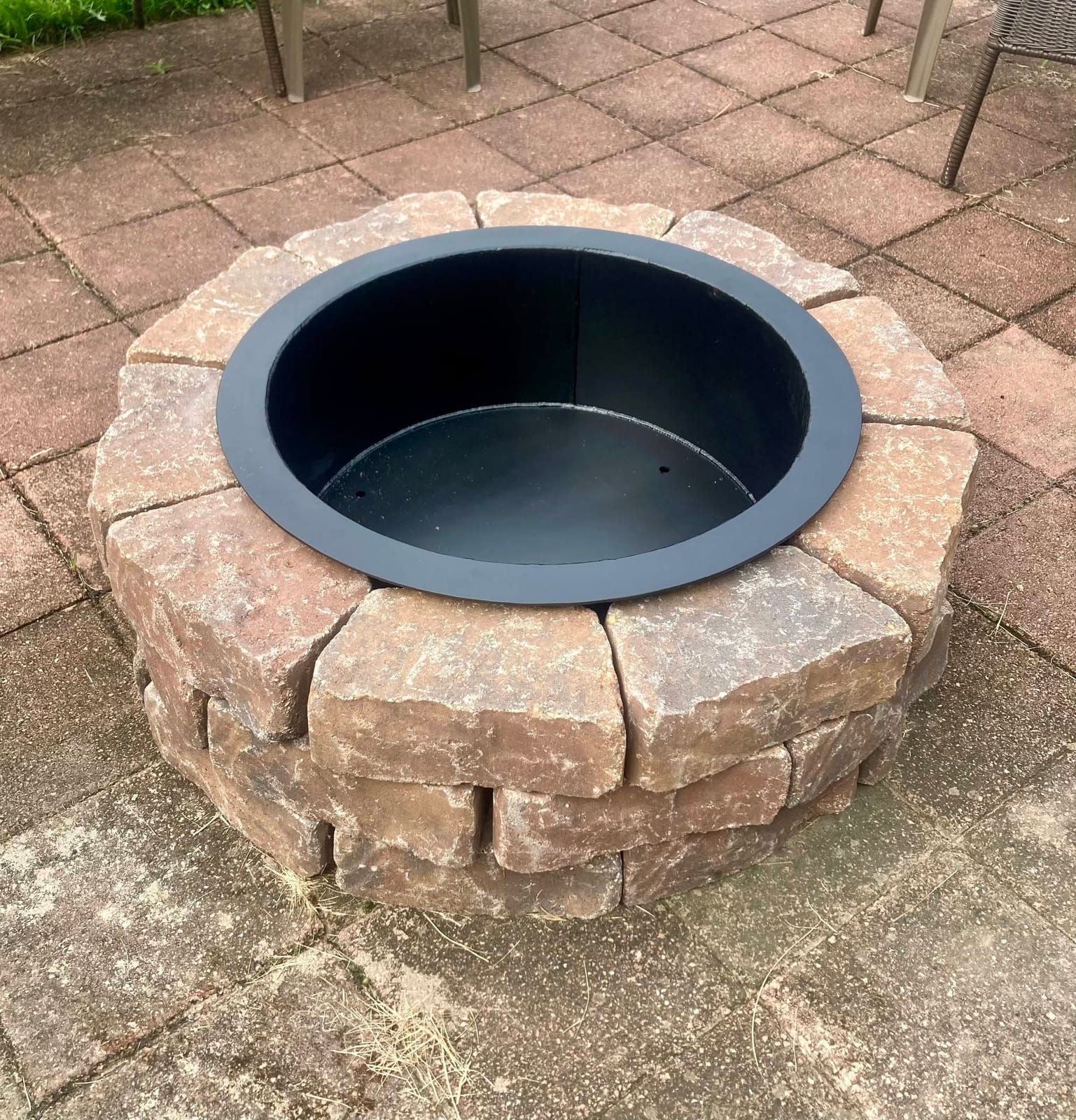 A custom rolled steel fire pit ring insert seated in a stone paver fire pit on a backyard patio