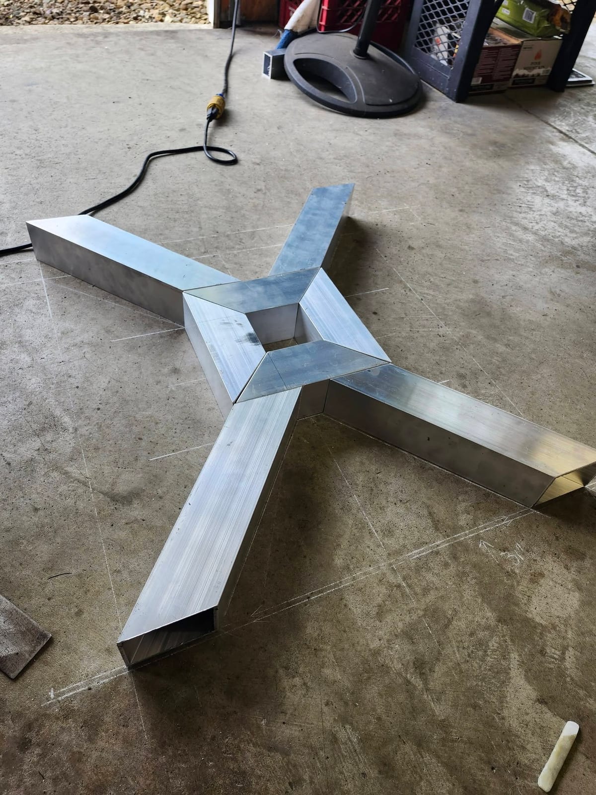 A four arm mitered box tube pedestal base laid out on the shop floor over its chalk layout lines