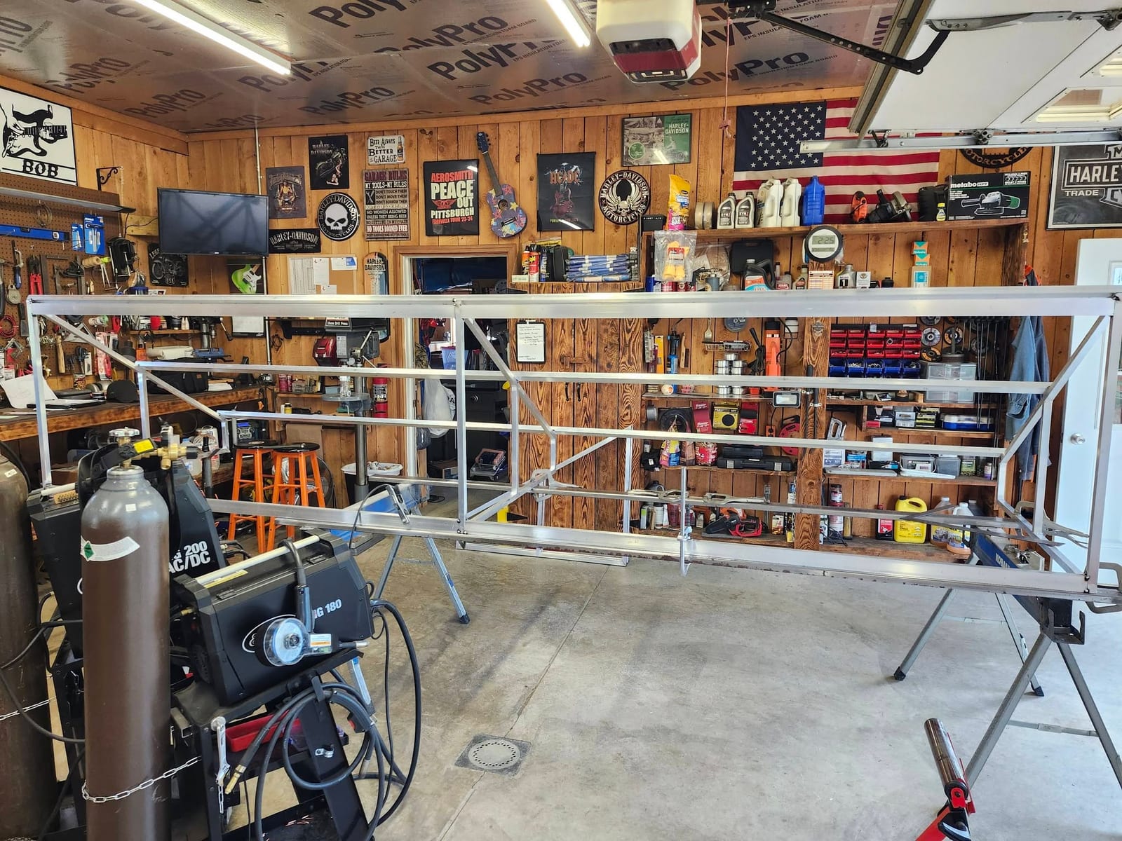 A long aluminum gate frame tacked up on sawhorses beside the TIG and MIG welders in the shop