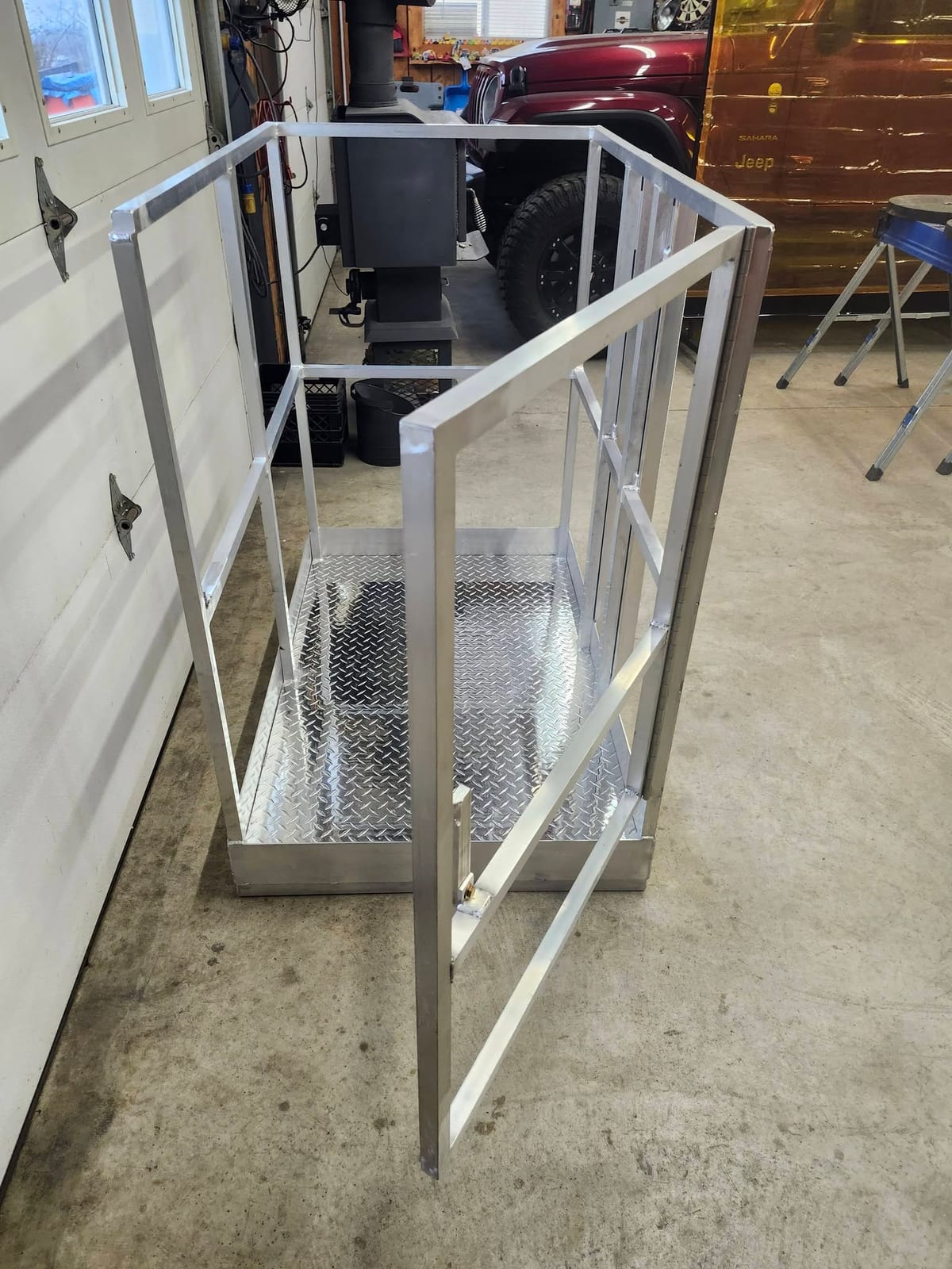 A finished aluminum man basket with a diamond plate deck and hinged safety gate, built for forklift use