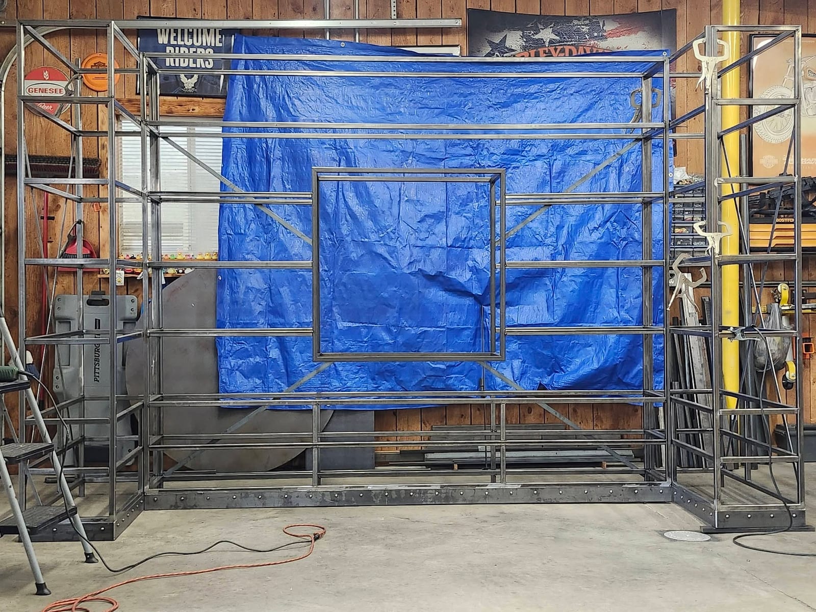 The bare welded steel frame of a custom built-in shelving wall standing in the shop before finishing